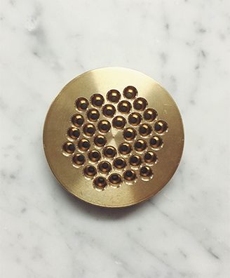 A brass die used to extrude the house-made pasta, resting on marble