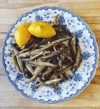 Fried smelts with lemon halves on a blue and white patterned plate