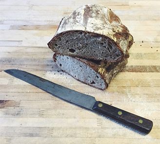 A cut loaf of dark crusty bread with a bread knife on a wooden board