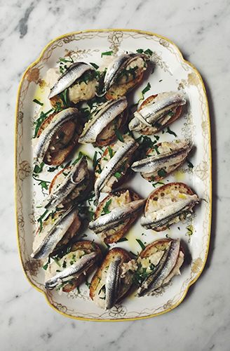 Marinated sardines on crostini with parsley and olive oil, served on a gilt-edged platter
