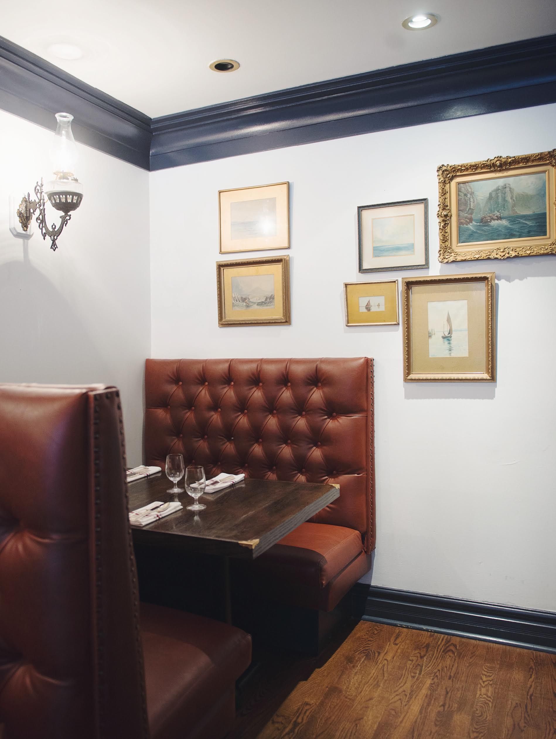 Corner booth in oxblood leather below a cluster of framed maritime watercolours and navy painted trim